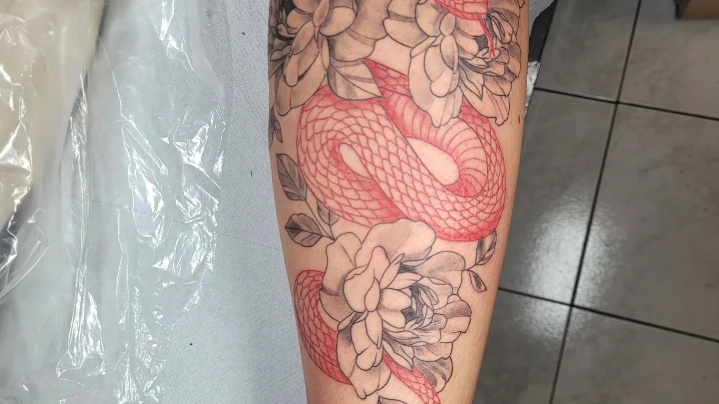 Tatouage d'un serpent rouge enroulé autour de pivoines noir et gris sur le bras, réalisé par Jean-Marie Joullié au salon JMJ Tattoo proche de Pézenas