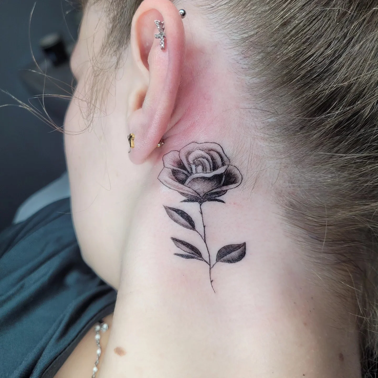 Tatouage fine line d'une petite rose derrière l'oreille, noir et gris délicat, réalisé par Jean-Marie Joullié au salon JMJ Tattoo proche de Portiragnes