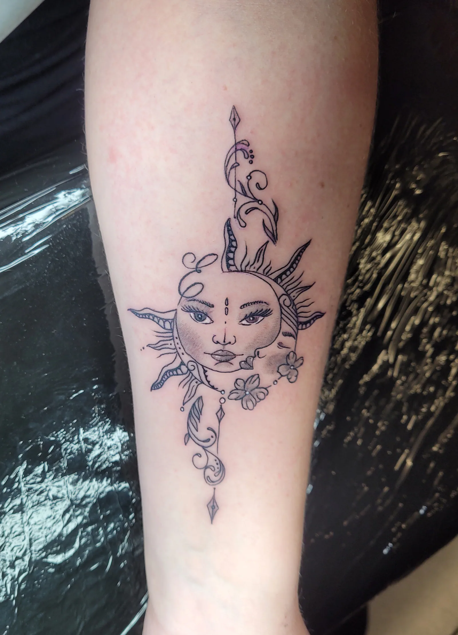 Tatouage fine line d'un soleil et d'une lune ornementaux sur l'avant-bras, réalisé par Jean-Marie Joullié au salon JMJ Tattoo à Béziers et Sérignan
