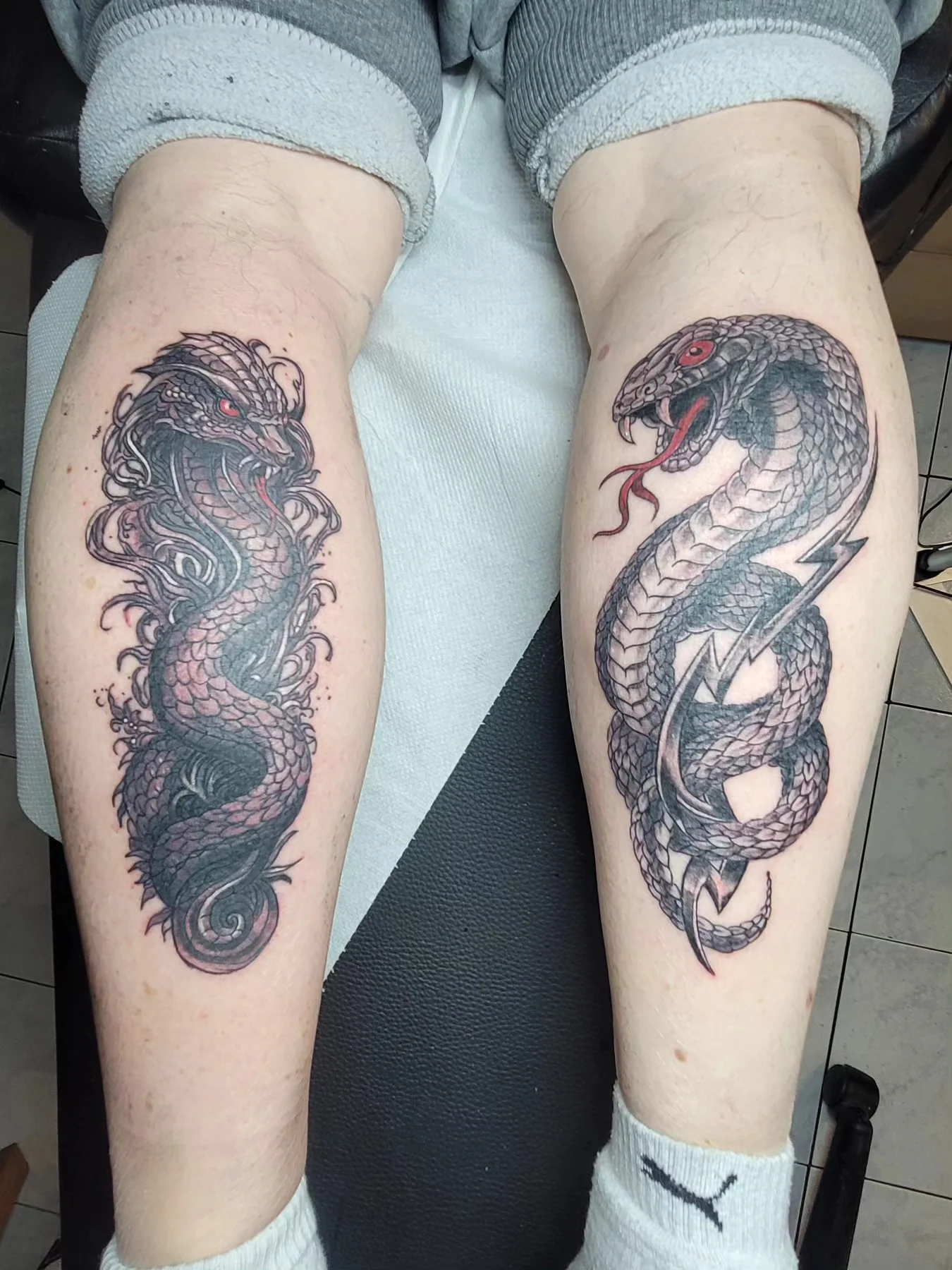 Deux tatouages japonais assortis sur les mollets, dragon et cobra en noir et gris avec détails rouges, réalisés par Jean-Marie Joullié au salon JMJ Tattoo proche de Cap d'Agde