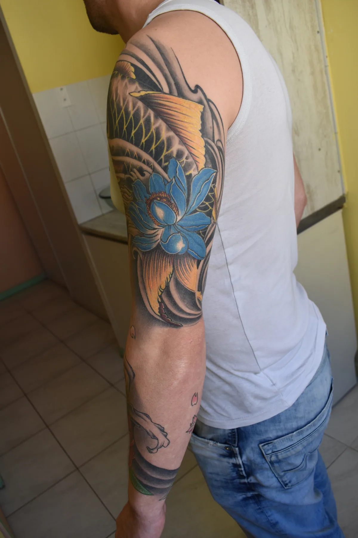Vue de profil d'une manchette japonaise : carpe koï yin-yang et lotus bleu sur le bras, descente vers l'avant-bras, réalisée par Jean-Marie Joullié au salon JMJ Tattoo proche de Marseillan