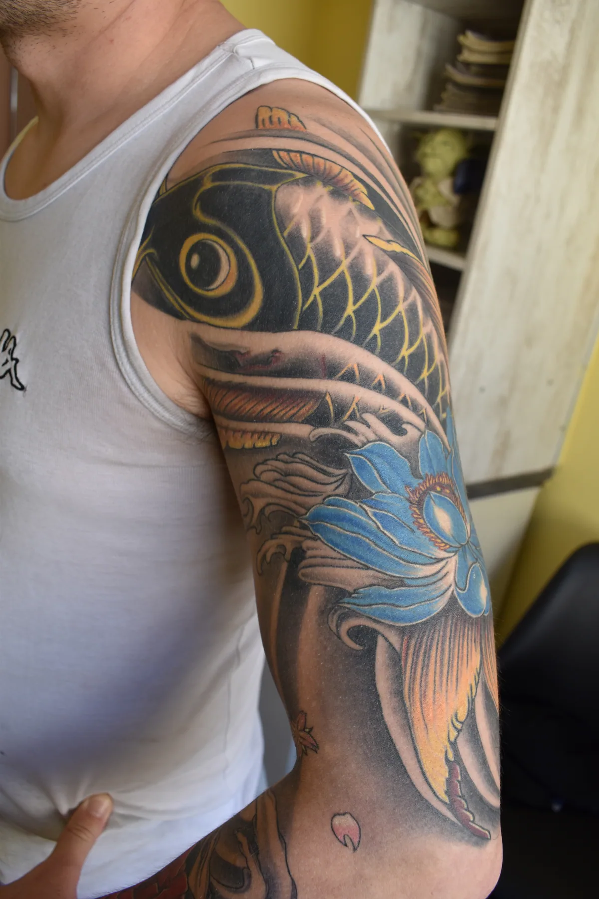 Manchette japonaise complète sur le bras représentant une carpe koï yin-yang noire et blanche, un lotus bleu en éclosion et des vagues, réalisée par Jean-Marie Joullié au salon JMJ Tattoo proche de Cap d'Agde