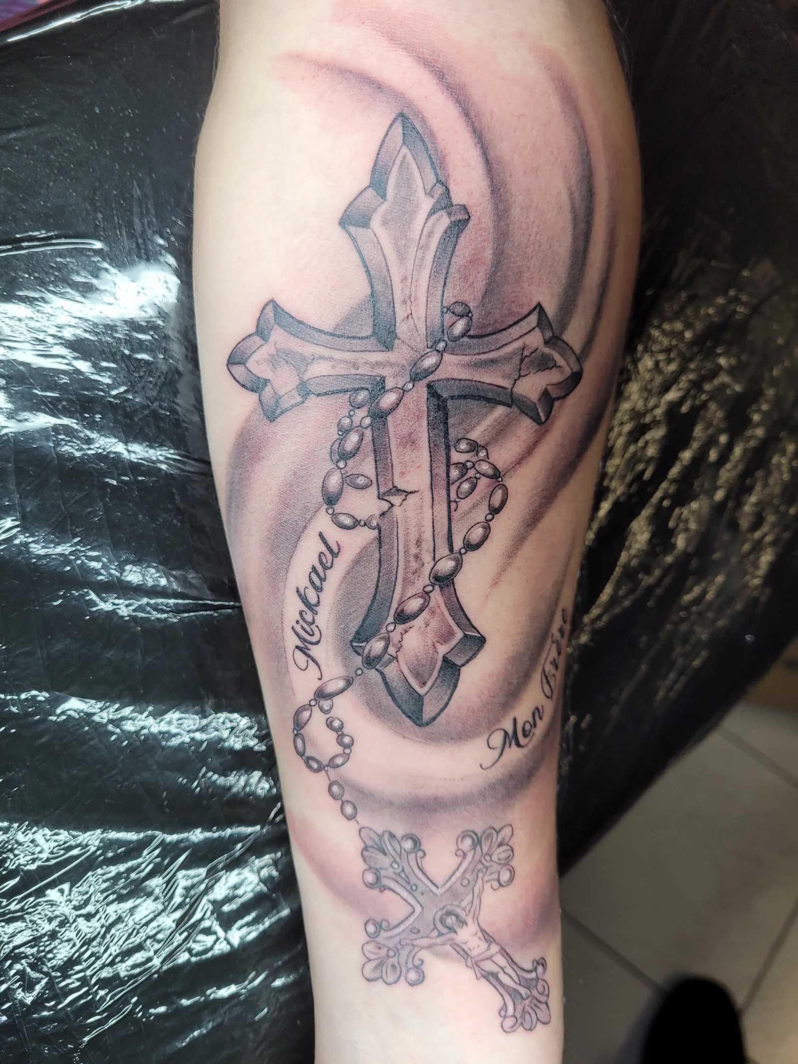 Croix et chapelet noir et gris sur avant-bras, travail repris — JMJ Tattoo Sérignan