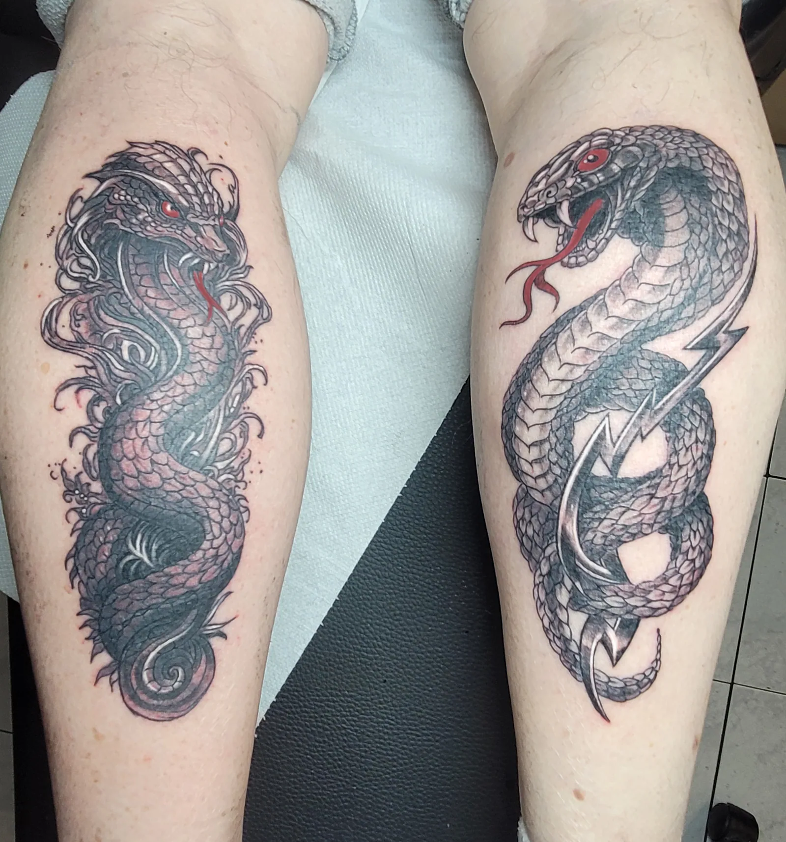 Tatouage noir et gris d'un dragon et d'un serpent entrelacés sur le mollet, réalisé par Jean-Marie Joullié au salon JMJ Tattoo à Béziers et Sérignan