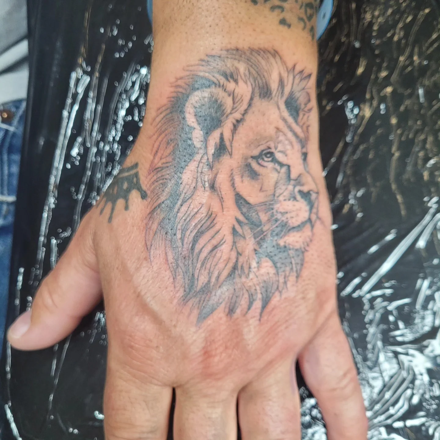 Tatouage réaliste d'un lion sur le dos de la main en noir et gris, réalisé par Jean-Marie Joullié au salon JMJ Tattoo proche de Valras-Plage
