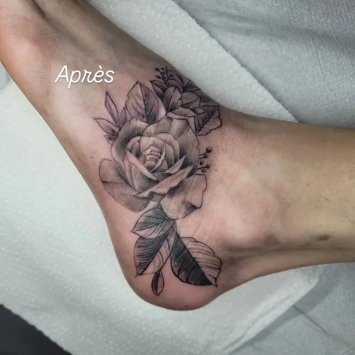 Après cover-up : rose réaliste noir et gris recouvrant l'ancien tatouage, composition adaptée à la cambrure de la cheville