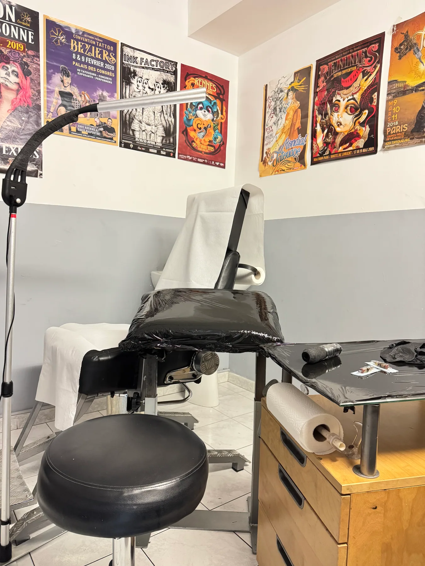 Poste de travail du tatoueur au salon JMJ Tattoo Sérignan, entouré d'un mur d'affiches de conventions tattoo