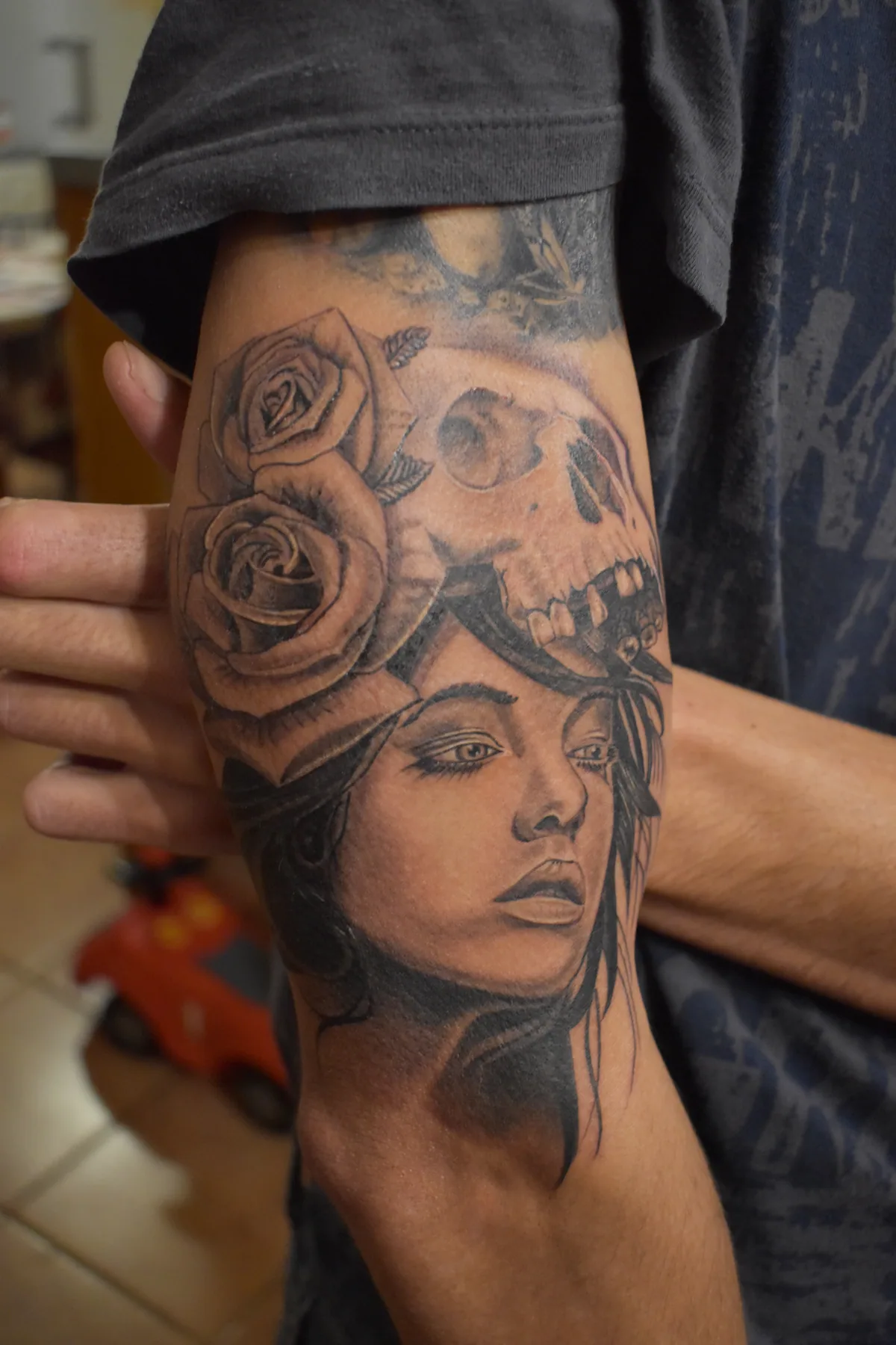 Tatouage sur mesure d'inspiration chicano représentant un visage de femme couronné de roses et d'un crâne, sur le bras en noir et gris, réalisé par Jean-Marie Joullié au salon JMJ Tattoo proche de Pézenas