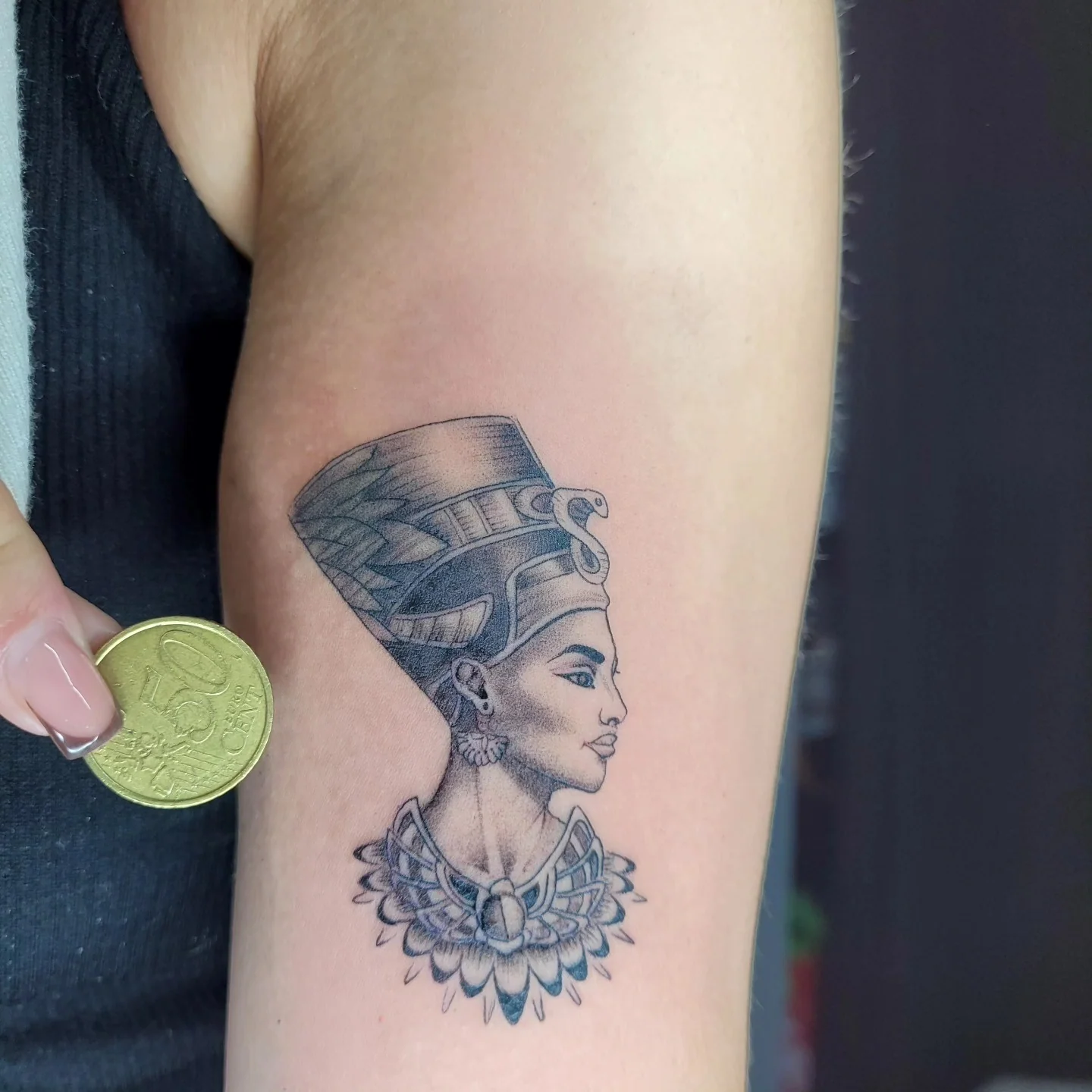 Tatouage d'un buste de Néfertiti avec coiffe égyptienne et collier ornemental, noir et gris sur le bras, réalisé par Jean-Marie Joullié au salon JMJ Tattoo proche de Pézenas